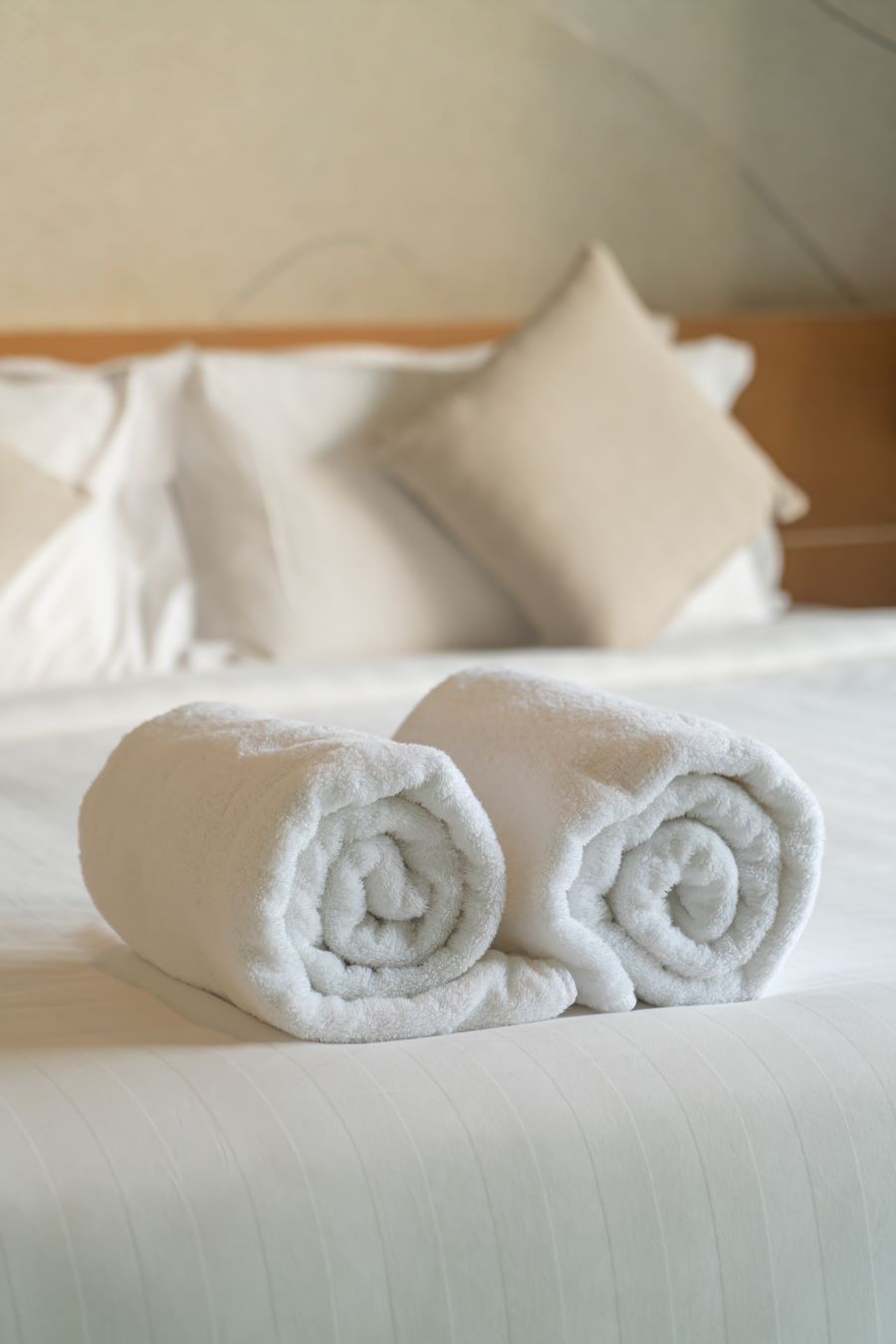 Rolled up towels on bed with white linens